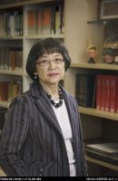 Chiaki Ajioka standing in front of bookcase in Asian Reading Room, reference tome and a few decorative items on the shelves
