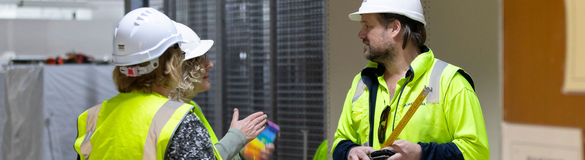 Two women and one man, all wearing high-visibility clothing and hard hats, having a discussion 