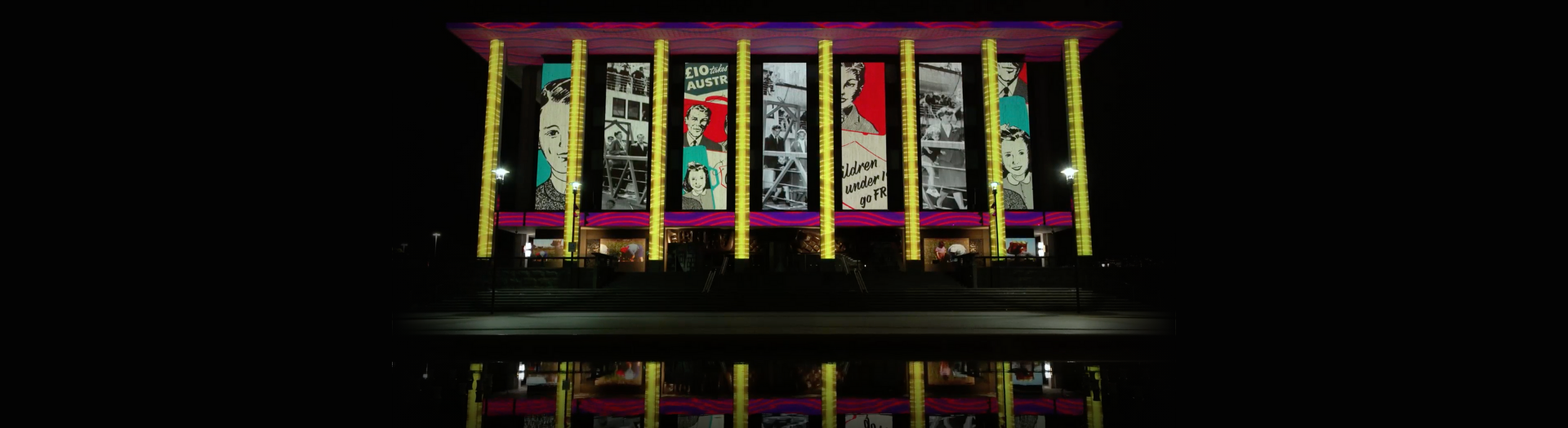 National Library building lit up with images projected onto it. They include a photo of people walking off a large ship, and advertisements for traveling to Australia