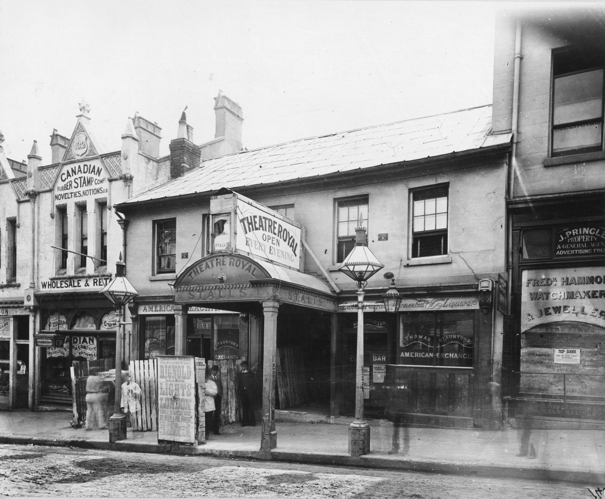 Black and white photograph of a row of shopfronts. One facade reads "Theatre Royal: Open Every Evening".