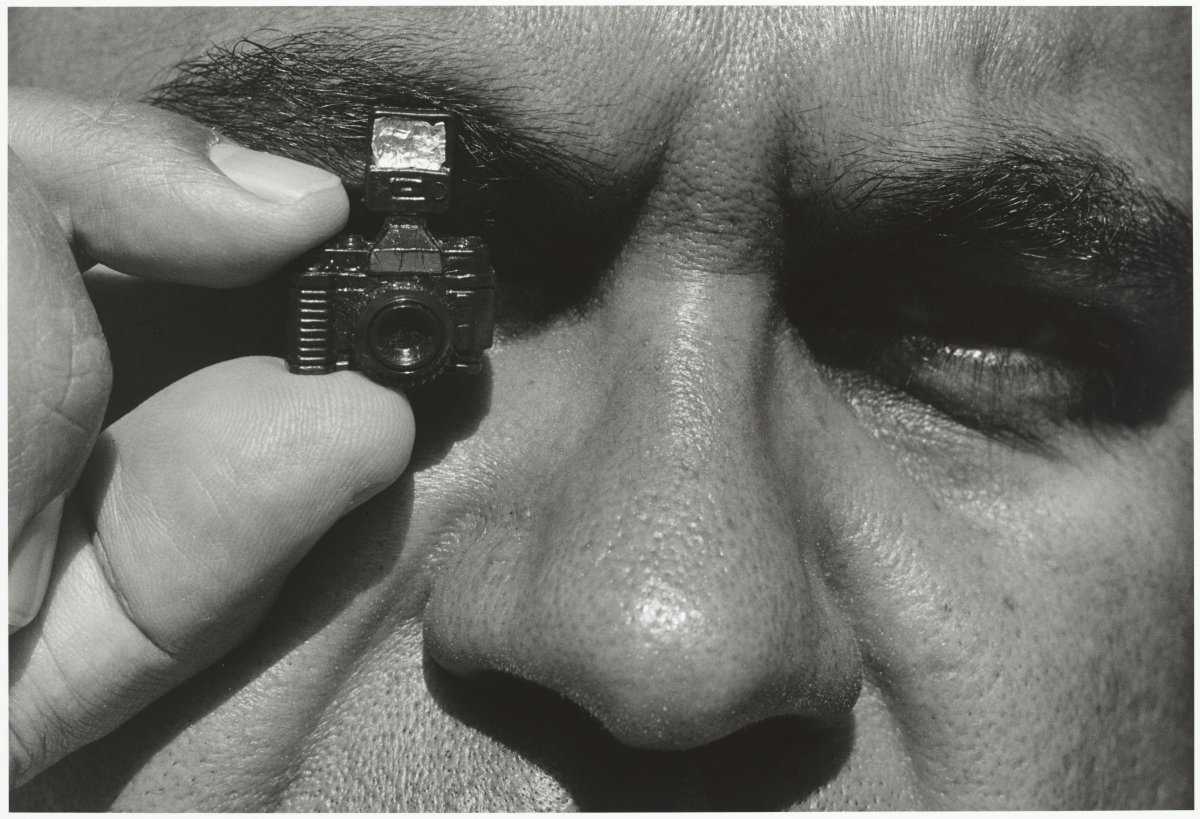 A black and white close up of a man's face showing from the brows down to just above the lip with a tiny camera covering the left eye 