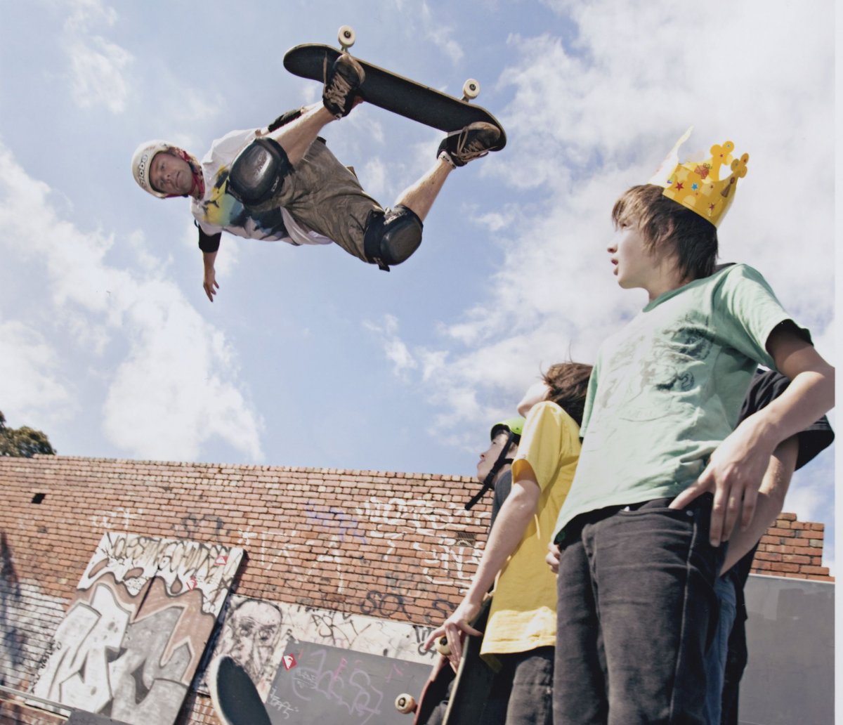 A man in the air doing a trick on a skateboard on the left with some young men watching him on the right