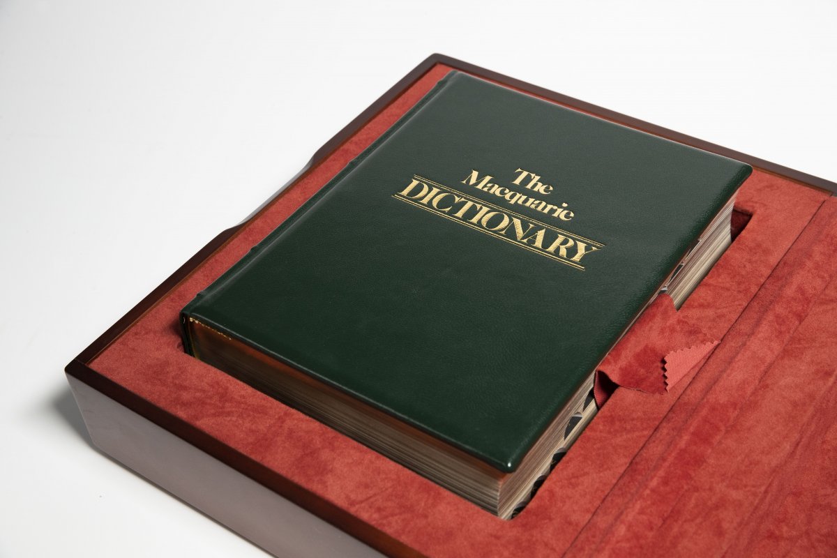 A rare old Macquarie dictionary sits closed in a box with red velvet and a dark wood case. 
