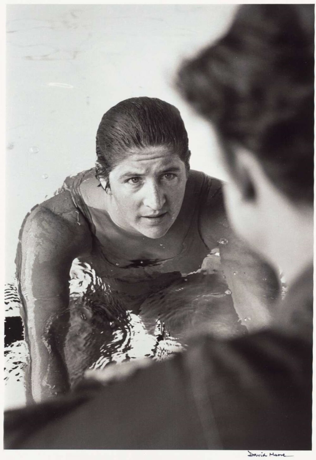 A black and white photo of Dawn Frazer looking up at a man from the pool, while she is talking to him.