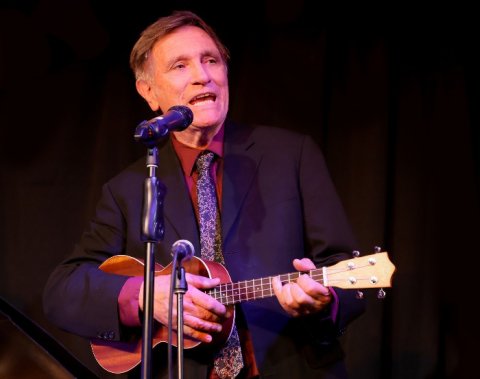 Man in a suit and tie playing guitar and singing behind two microphones
