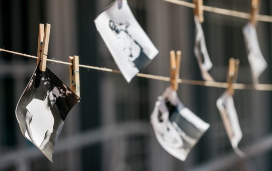 Black and white photographs hanging on two rows of twine, being held up by wooden pegs.