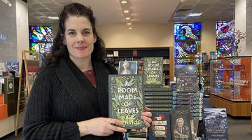 Lynda standing in front of bookshop hold A Room Made of Leaves book
