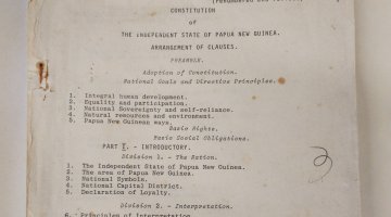 An old, weather piece of paper that has typewriter text on it detailing the first few parts of the fourth drafts of the Constitution of Papua New Guinea