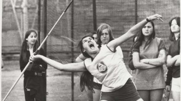 A black and white photo of a girl leaning back to throw a javelin while yelling.
