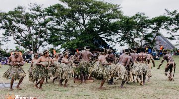 Dance group of men and women from Vanuatu performing a dance outside wearing grass skirts and dresses
