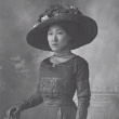 A black and white photograph of a Chinese Australian woman dressed in an 1800s dress and hat