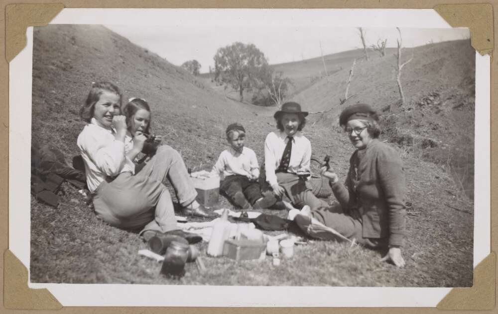 Children smile at the camera as they enjoy an outdoor picnic with hills in the background