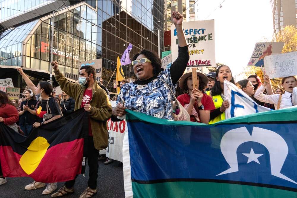 A group of protesters brandishing placards and holding the Torres Strait and Aboriginal flags march in the streets of Melbourne with their fists raised during the School Strike for Climate Rally in May 2021.
