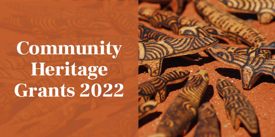 Painted wooden objects are arranged on red sand. A text overlay reads "Community Heritage Grants 2022"