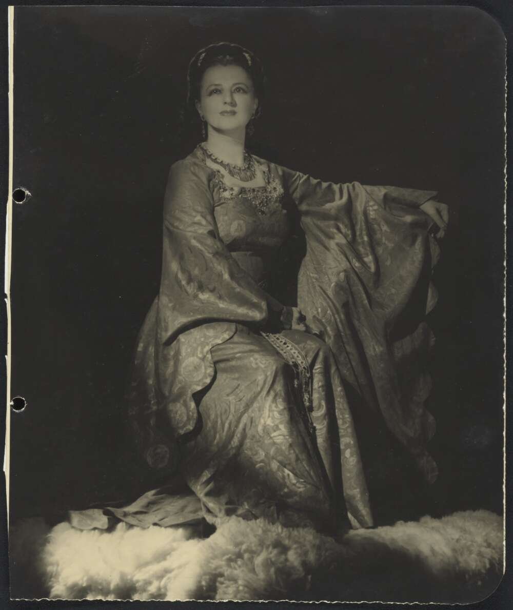 Dark photograph of a woman posed in a long dress and jewellery.