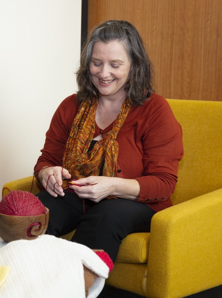 A woman sitting on a yellow couch and knitting.