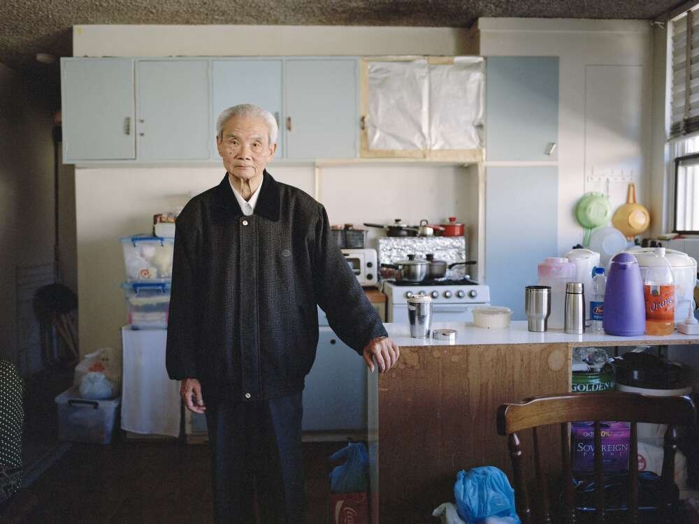 A man stands in a cluttered kitchen with broken cabinet doors