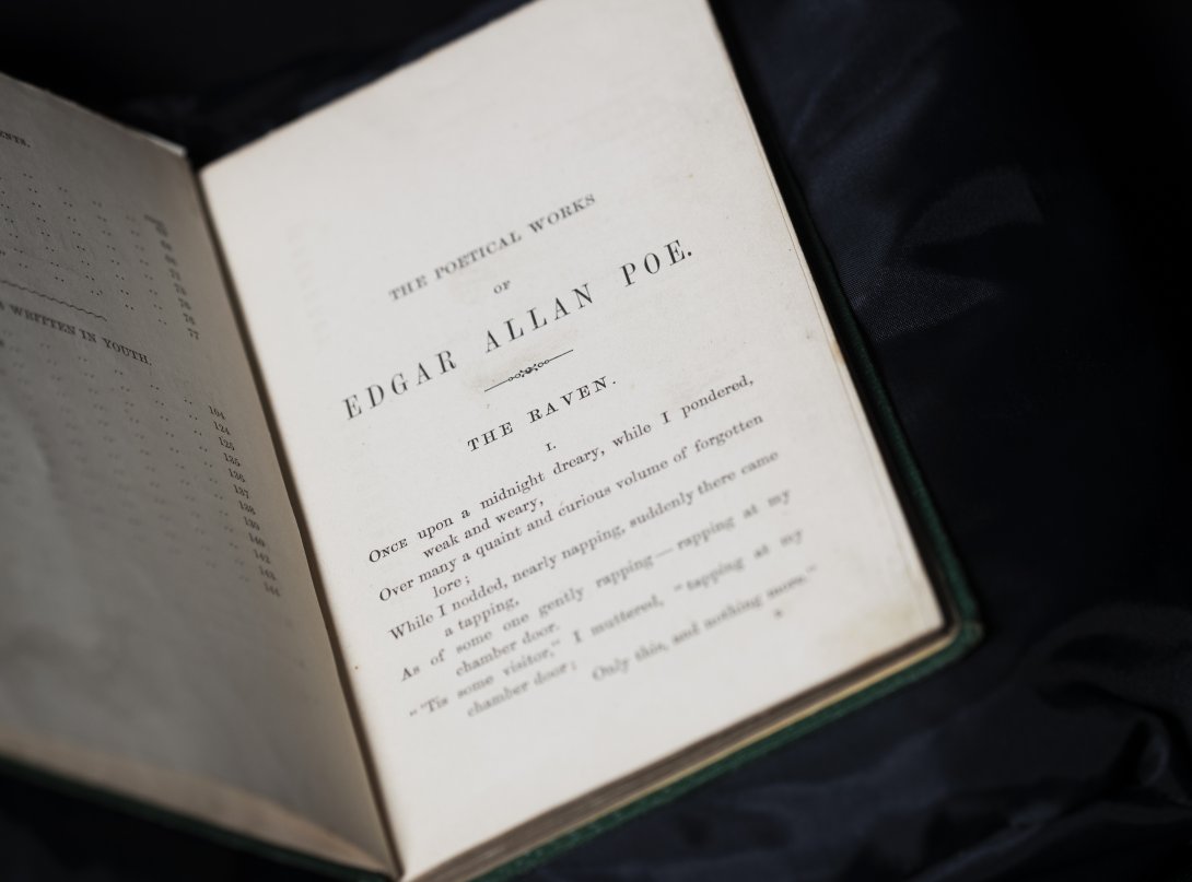 An open book showing the page with 'The Raven' poem showing. Text from top to bottom: 'The poetical works, Edgar Allen Poe, The Raven' and continues with the start of the poem. 