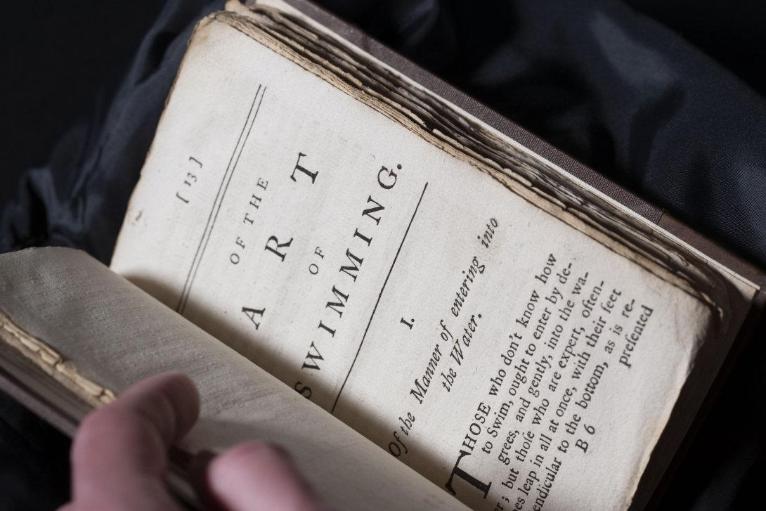 A rare book about swimming held open. Visible page is a page of text with the title 'The Art of Swimming'.