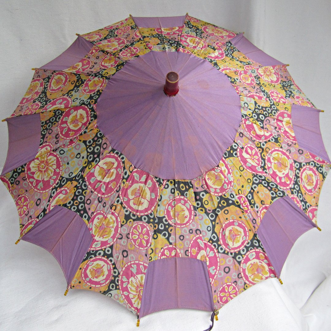A vintage silk women's umbrella or parasol, which is opened and has alternating panels of mauve and floral design.