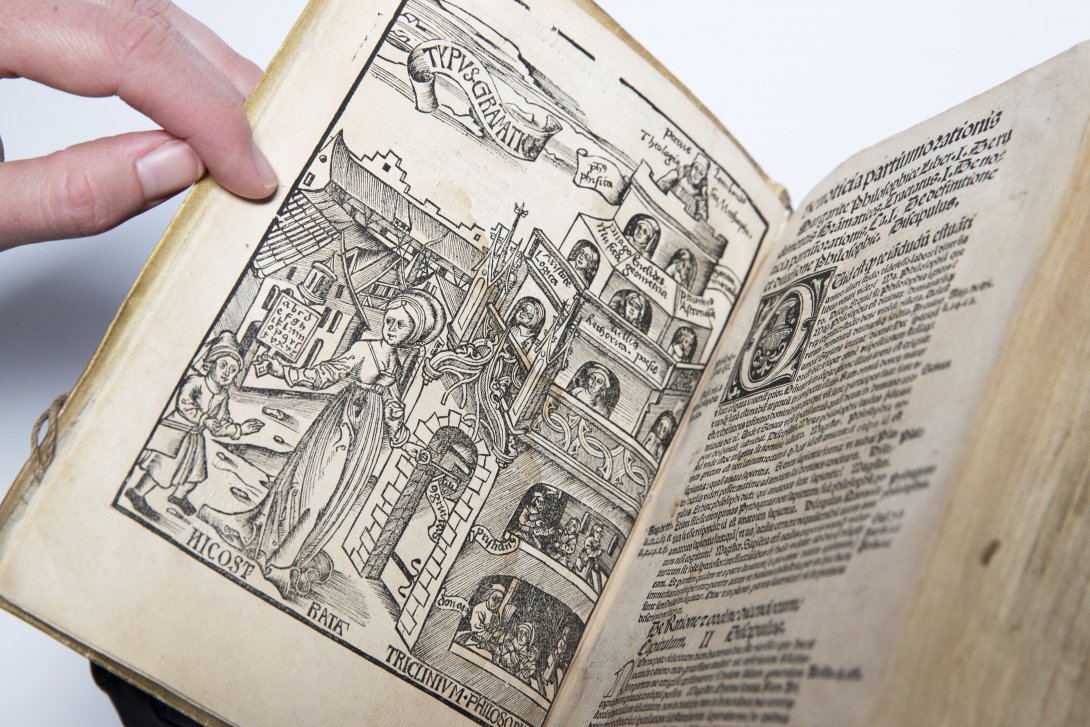 A rare book opened to show an illustration of people and a triangular tower on the left and a page of words on the right.