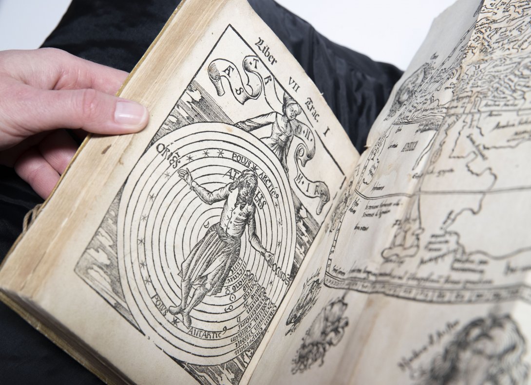 A rare book opened to a page with an illustration of a person standing in front of a spiral on the left and a illustrated map on the right. 