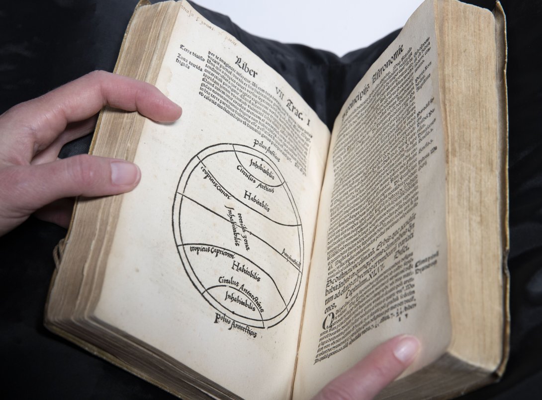 A rare book being held open to show some text and a circle with lines inside on the left and more text on the left. 