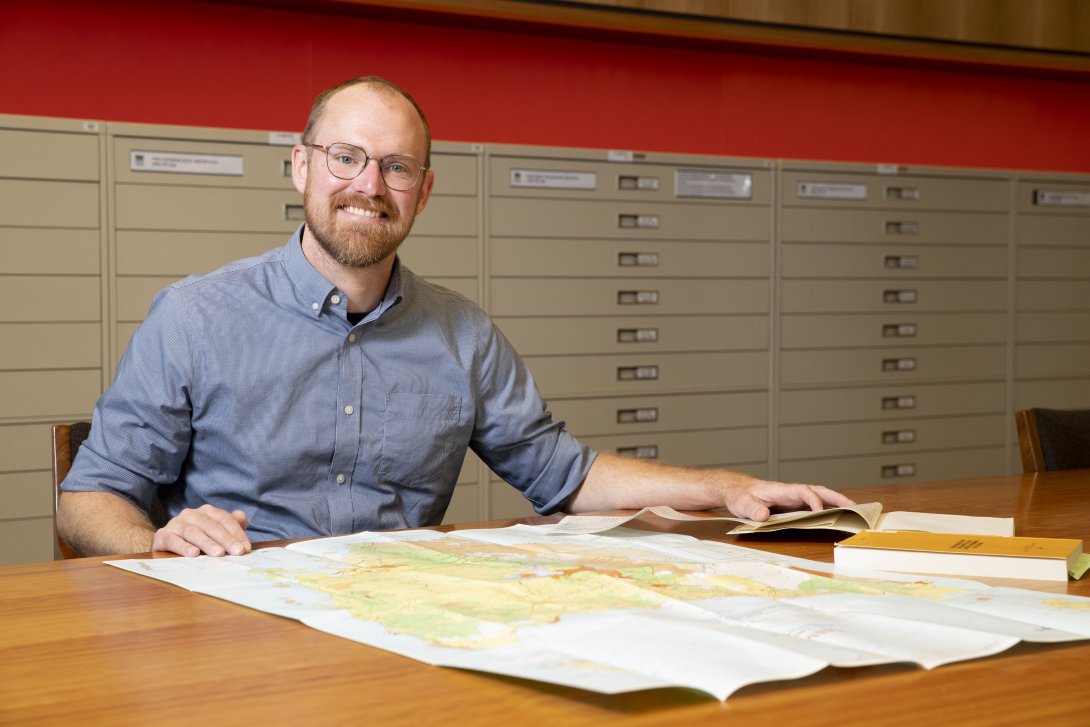 Image of NLA fellow Adam Sundberg sitting at a table with a large map