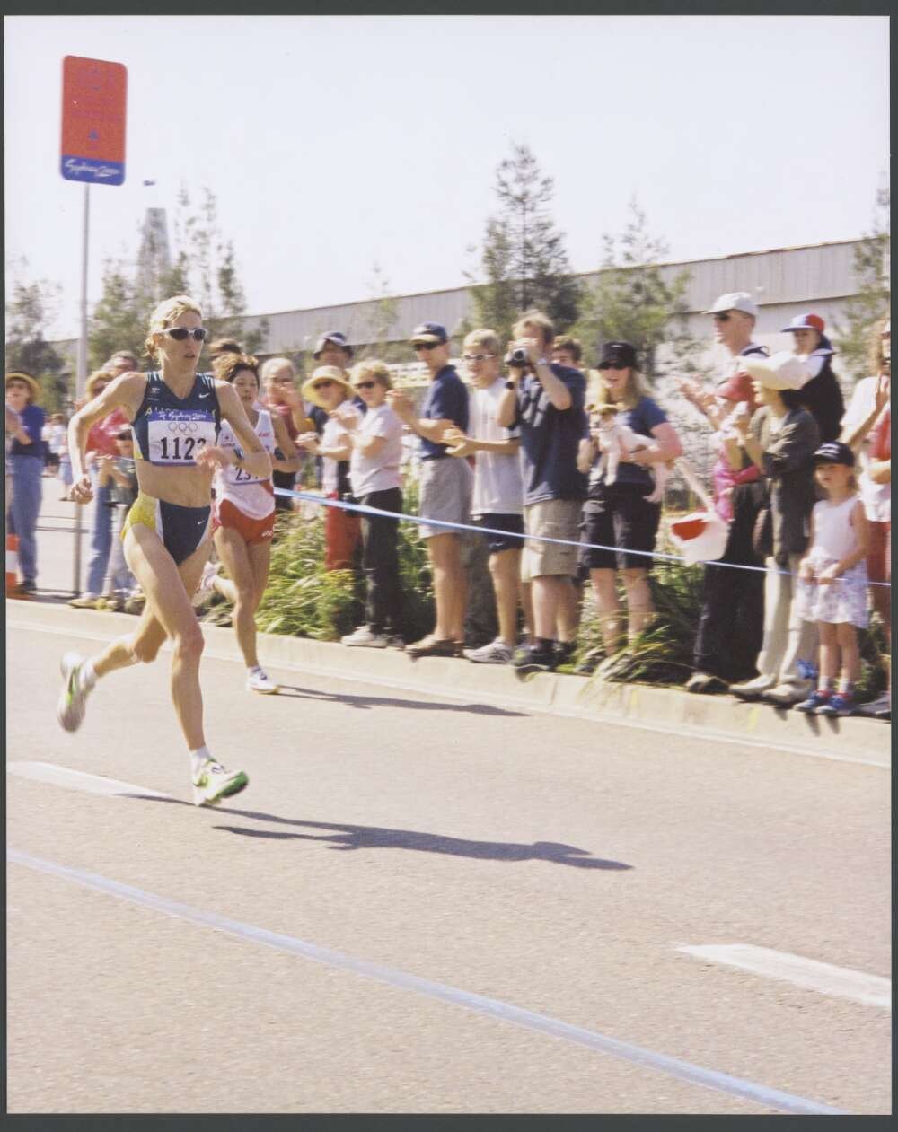 Woman participating in a marathon, with supporters of all ages standing along the road, including a woman holding a small dog
