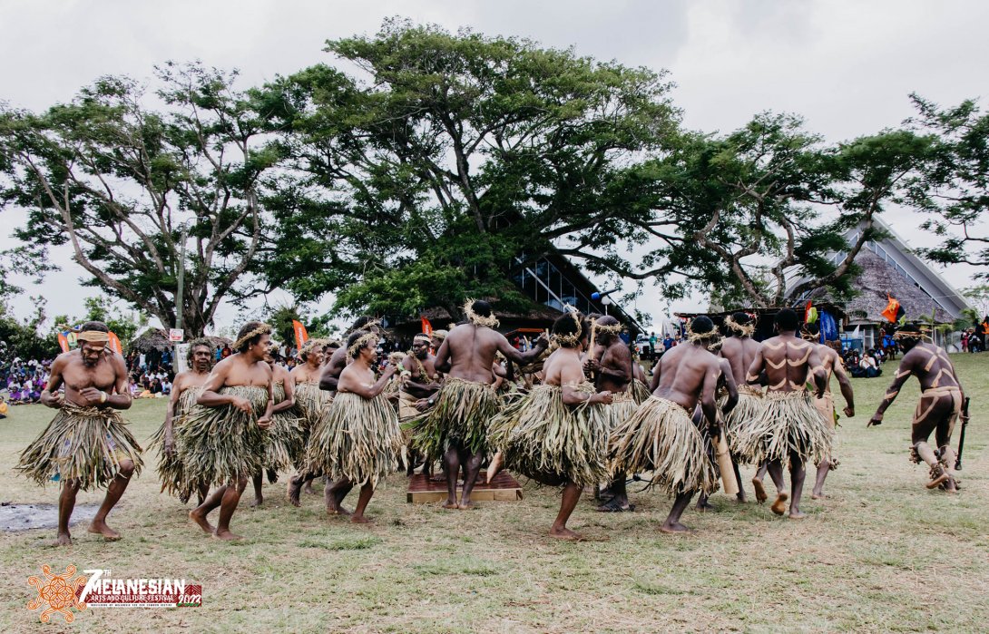 Dance group of men and women from Vanuatu performing a dance outside wearing grass skirts and dresses