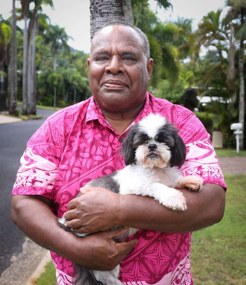 Fijian man in bright pink shirt smiling and holding a small white and black dog