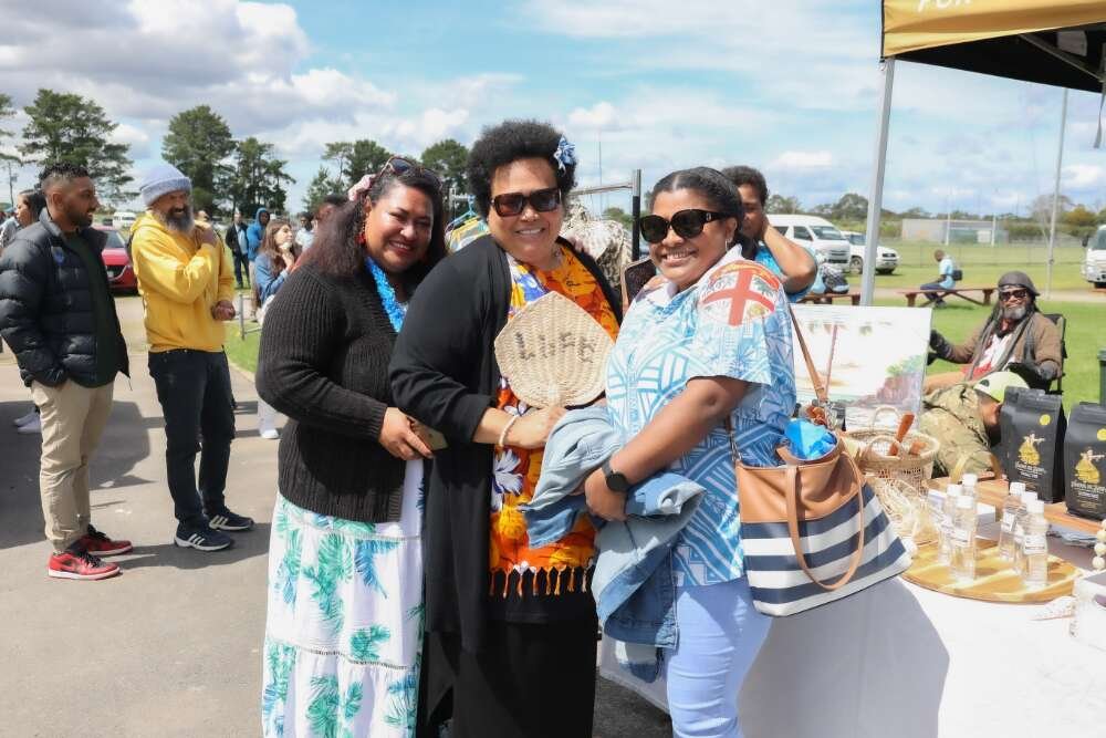 Three Fijian women smiling next to a stall at the Multicultural Festival