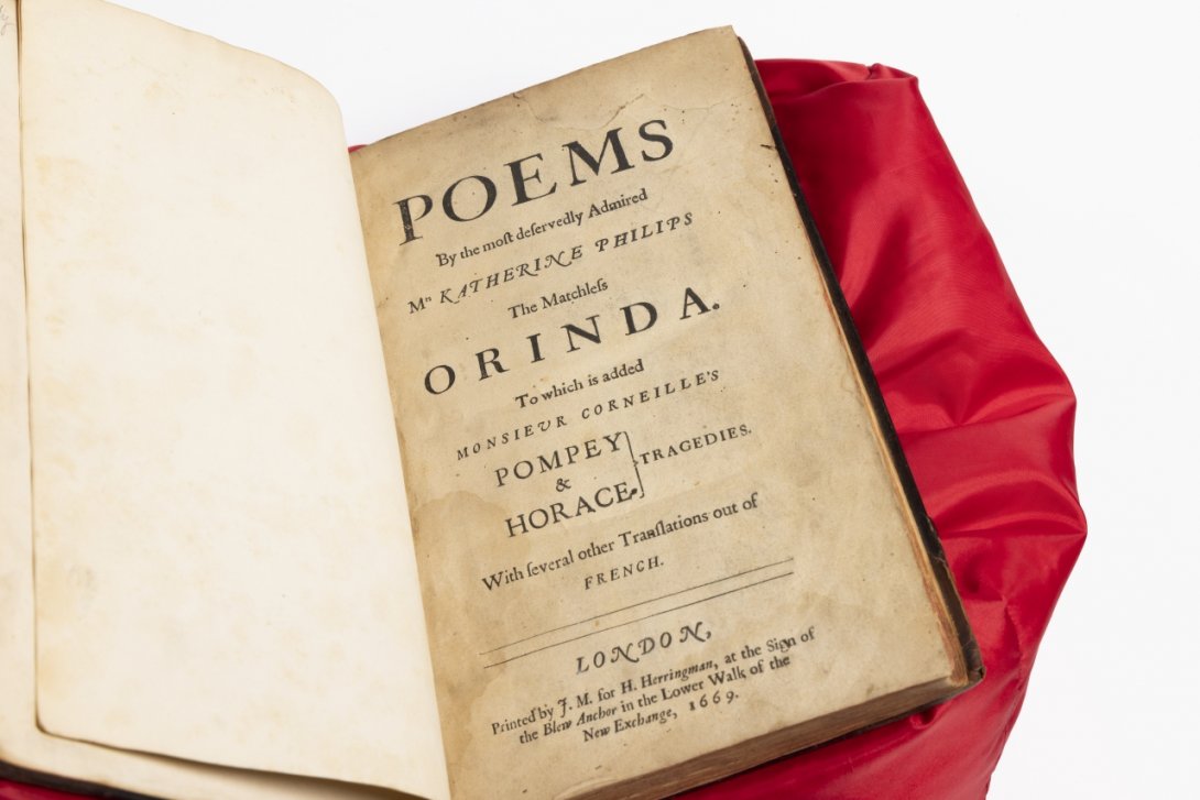 Photo of a rare book sitting on a red cushion open to the title page with 'POEMS' in large letters