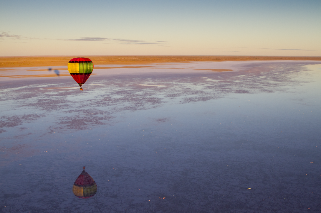 Hot air balloon flying over a huge lake and desert area that stretches out towards the horizon at dawn 