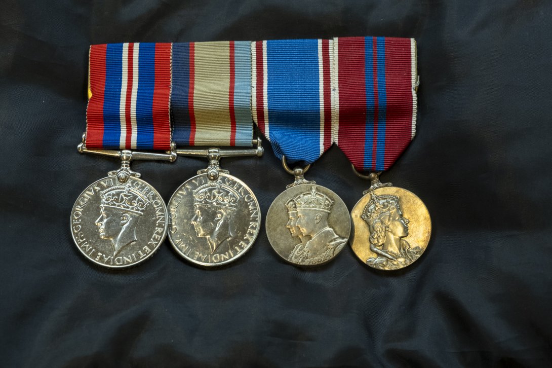 Four medals on a black fabric surface. The ribbons of the medals are various colours, mostly red and blue, and the medals themselves are engraved with a portrait