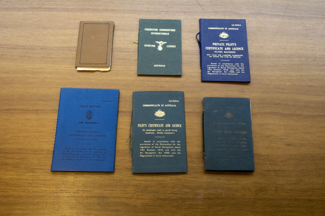Four small, thin books of various colours (blue, green and brown) sitting on a wooden table