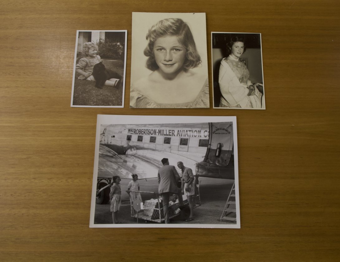 Photographs of various sizes on a wooden table. Three of the photos show a woman at various time in her childhood, and the fourth shows her and another girl with two men 