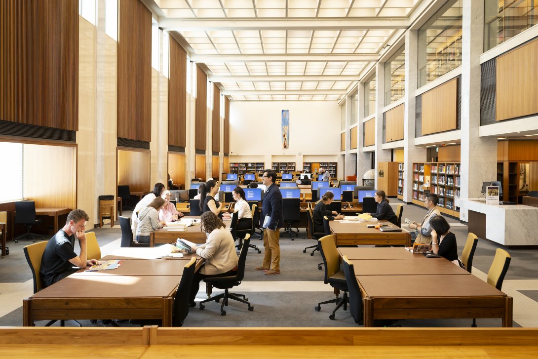 People reading and talking in a large, sunny room at tables, desks and computer stations