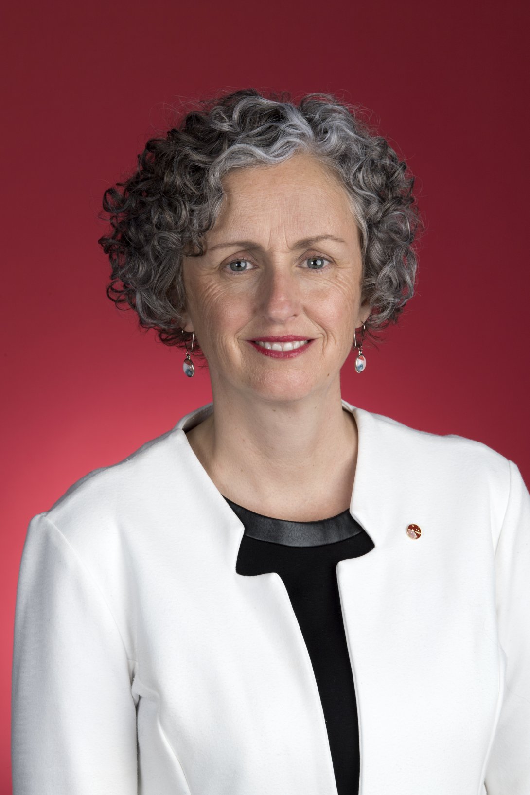 Photo portrait of woman with short curly hair wearing a black shirt and white blazer smiling