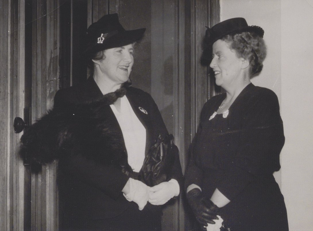 Two well-dressed women, Enid Lyons and Dorothy Tangney, standing and chatting