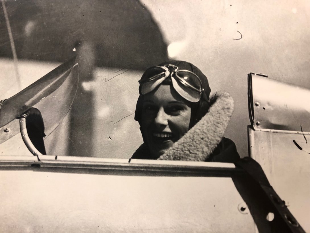 Woman, Jean Batten, sitting in the cockpit of a small single-person plane smiling