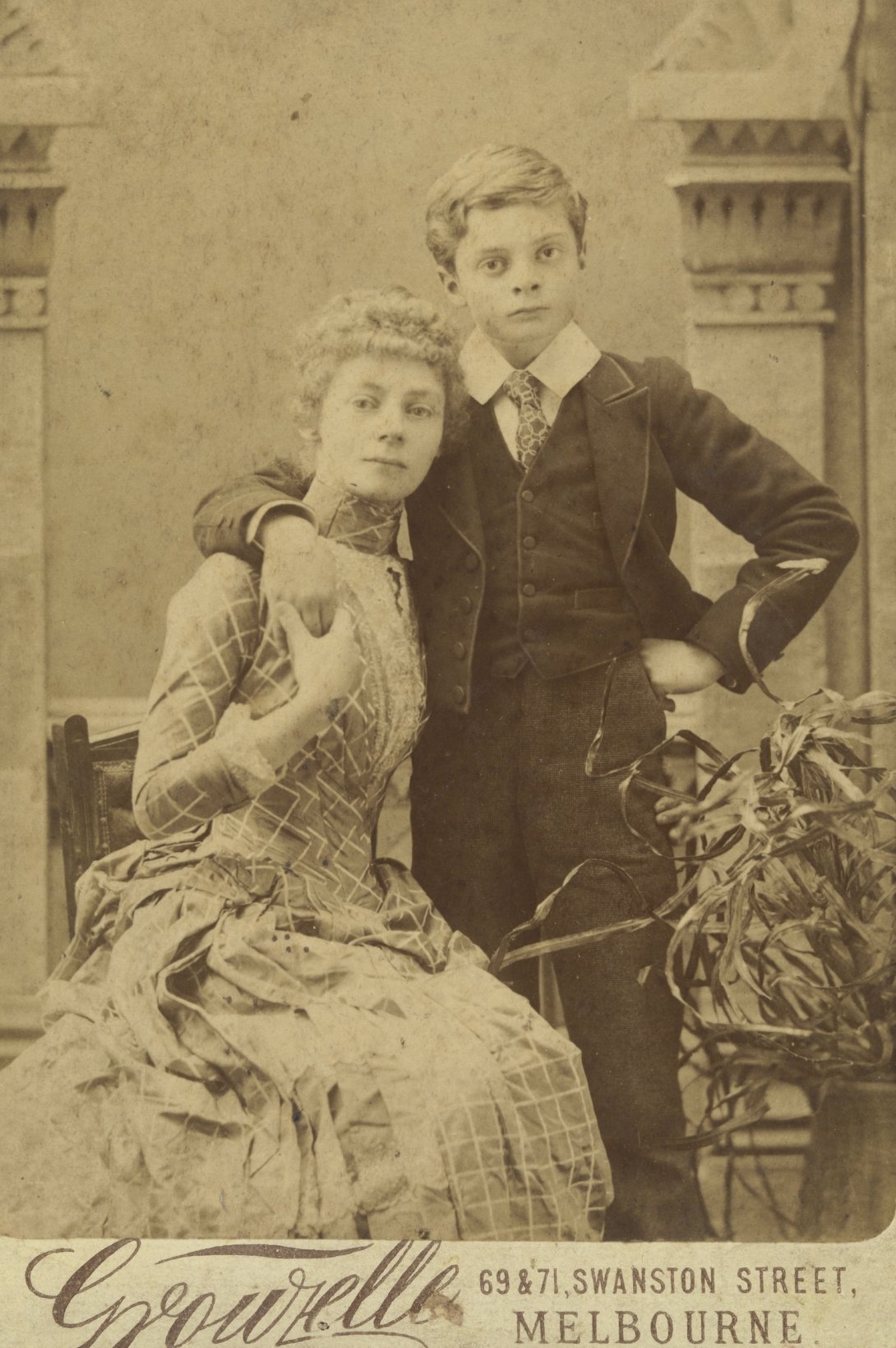 Sepia-toned photo portrait of artist Ellis Rowan and her young son, both dressed in formal attire.