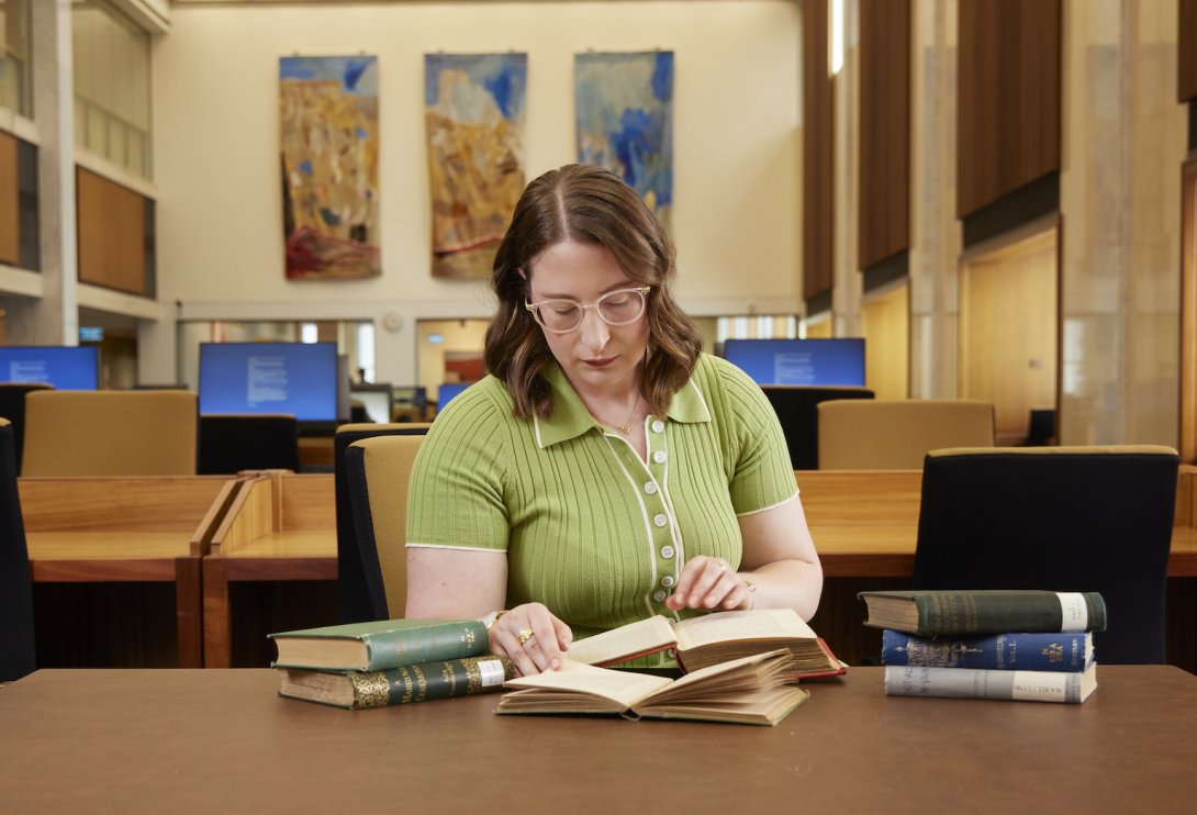 Zoe Smith, an NLA Scholar, sitting and reading at a table in the Main Reading Room with several books